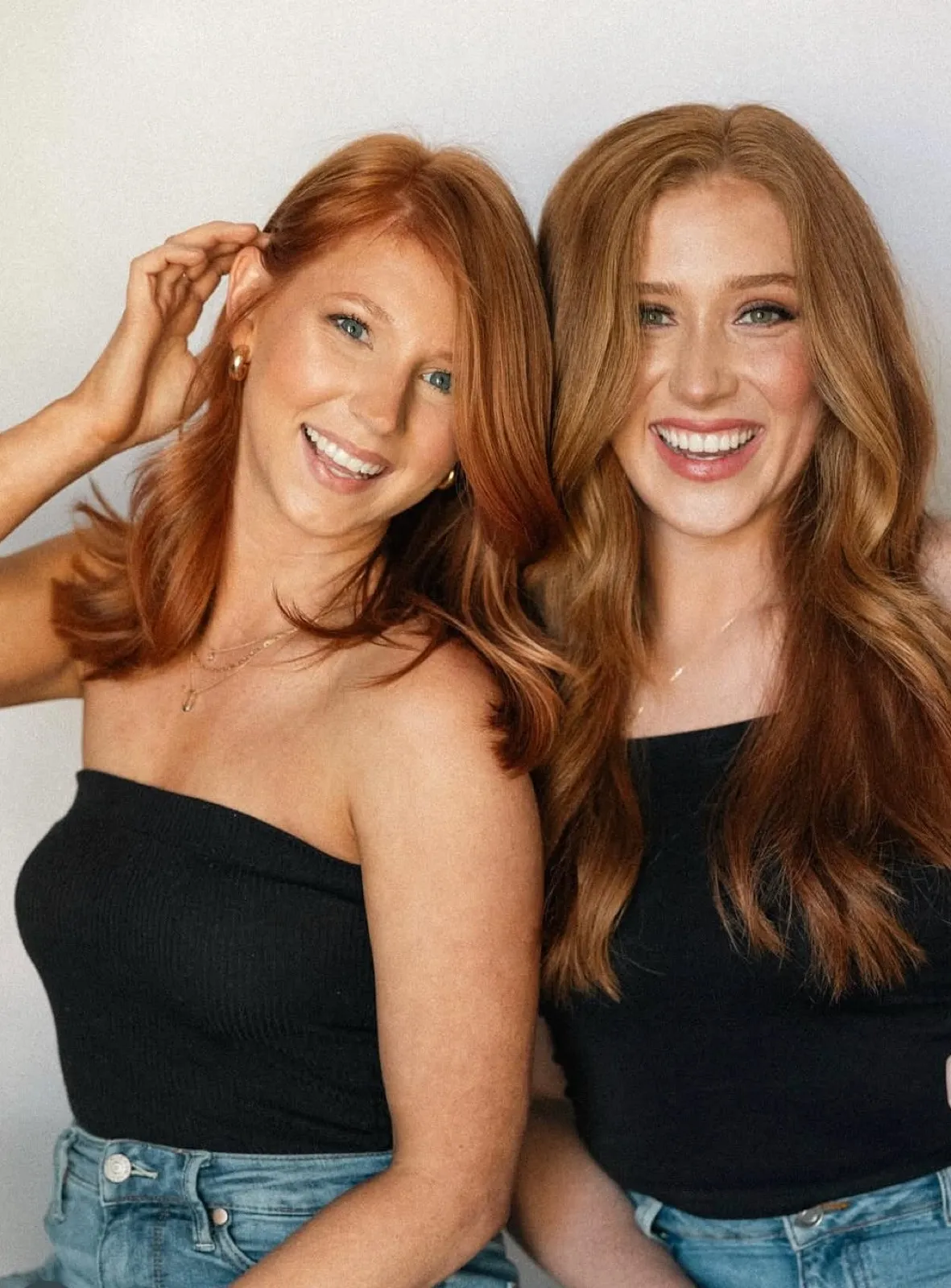 Two stylists with copper and auburn hair, black tops and denim